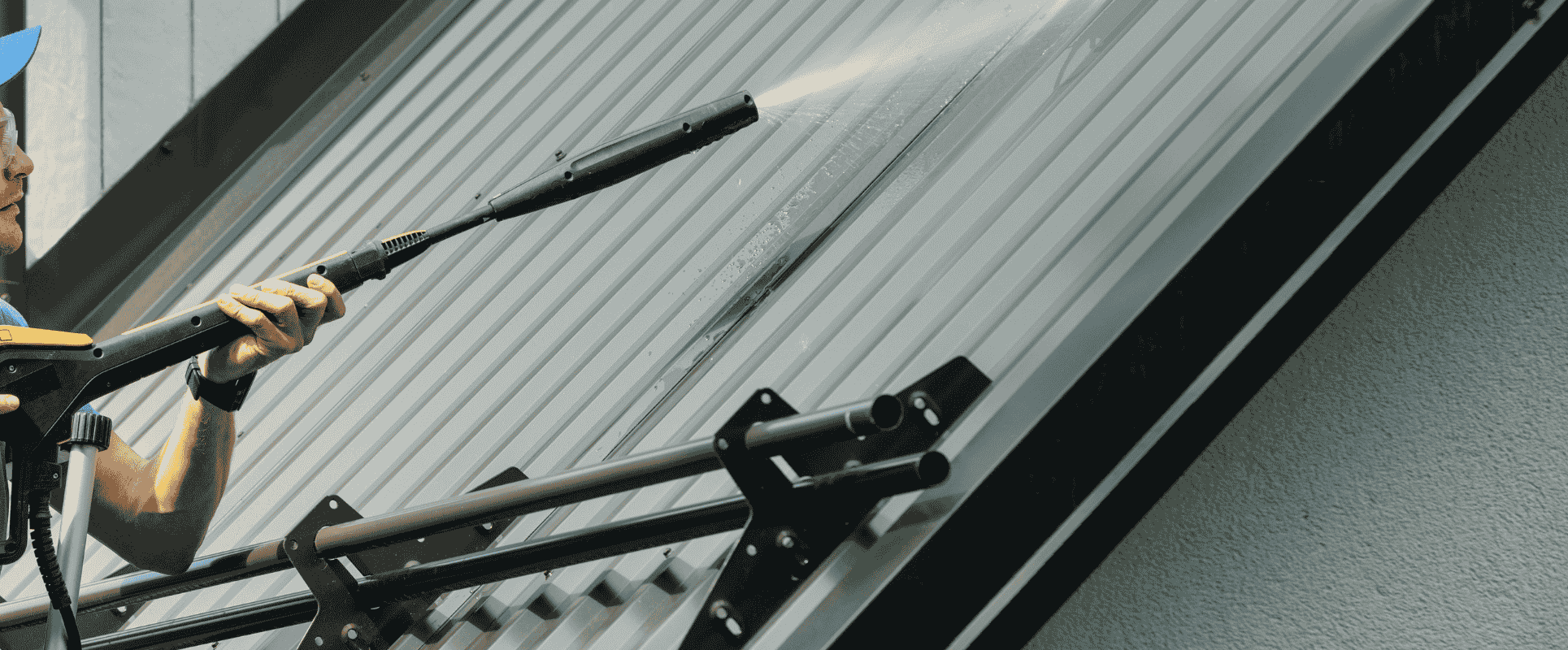 Roof cleaning with a pressure washer on a metal roof.