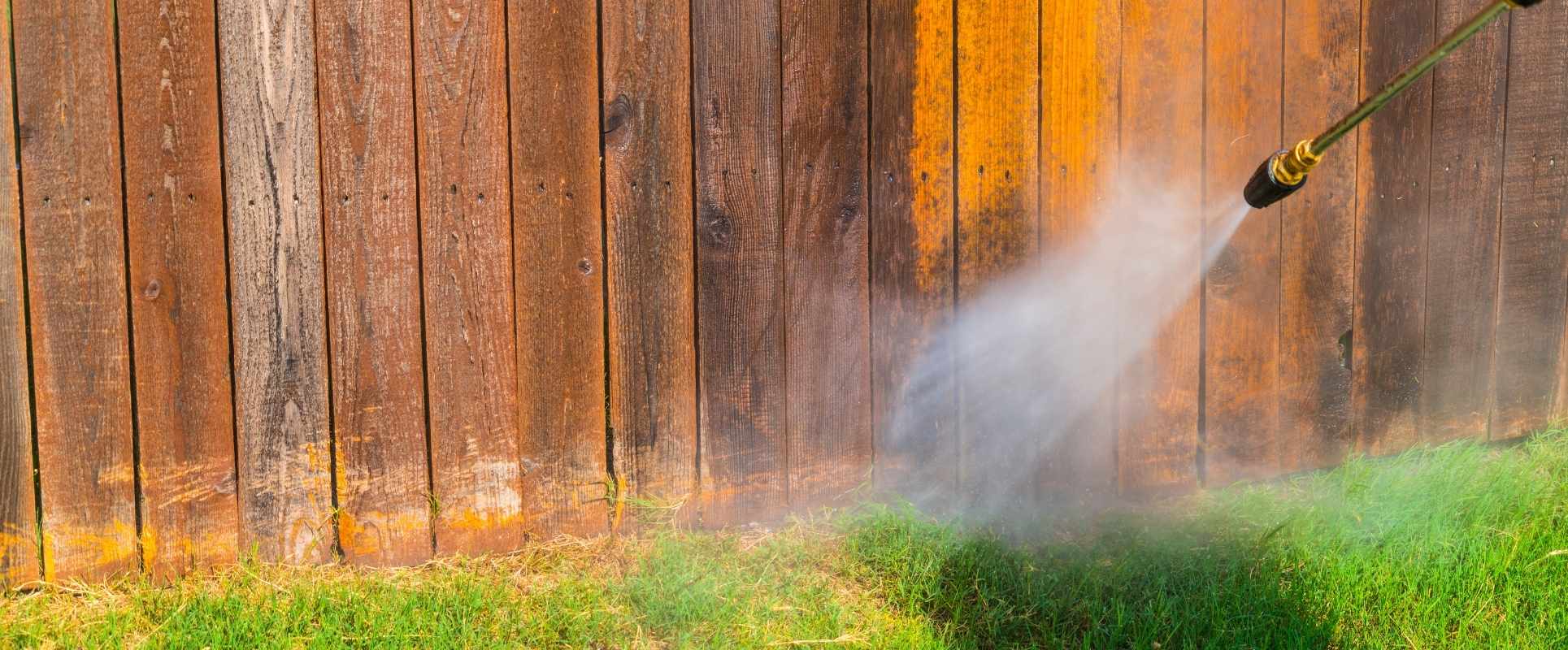 Pressure washing a wooden fence to remove dirt and discoloration.